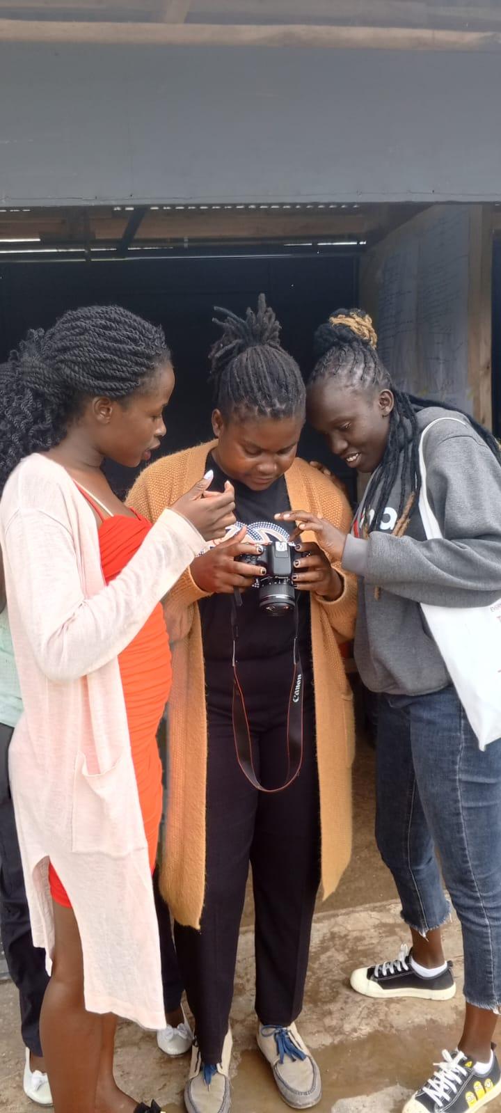 Three Ganjisha students reviewing photos on a Canon camera together